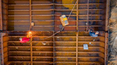 İşçiler eski büyük bir gemiyi keserken, mavnayı parçalara ayırırken, paslı metali kırbaç için keserken, asetilen meşalesi, geri dönüşüm, kıvılcımlar uçuşurken, üst görünümde işçiler görülüyor..