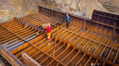 İşçiler eski büyük bir gemiyi keserken, mavnayı parçalara ayırırken, paslı metali kırbaç için keserken, asetilen meşalesi, geri dönüşüm, kıvılcımlar uçuşurken, üst görünümde işçiler görülüyor..