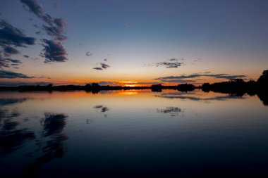 Akşamları güzel günbatımının manzarası gölün üzerinde, gölün üzerinde siluet suyun üzerinde ve bulutların sakin sularda yansıması.