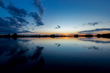 Akşamları güzel günbatımının manzarası gölün üzerinde, gölün üzerinde siluet suyun üzerinde ve bulutların sakin sularda yansıması.