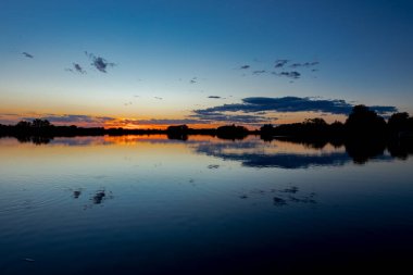Akşamları güzel günbatımının manzarası gölün üzerinde, gölün üzerinde siluet suyun üzerinde ve bulutların sakin sularda yansıması.