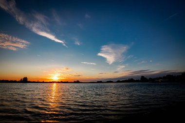 Akşamları güzel günbatımının manzarası gölün üzerinde, gölün üzerinde siluet suyun üzerinde ve bulutların sakin sularda yansıması.