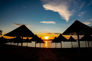 Akşamları güzel bir gün batımı manzarası gölün üzerinde, gölün üzerinde siluet suyun üzerinde ve bulutların sakin sularda yansıması. Thatched plaj şemsiyesi ahşap ve sazlıktan yapılır..