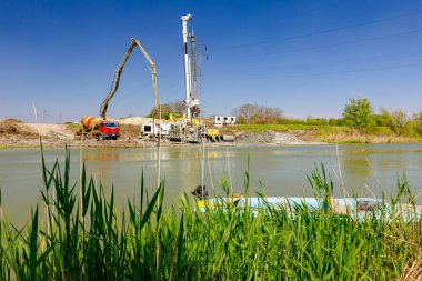 Endüstriyel kule sondaj makinesi, yere büyük aletler yığmak. Pompalı kamyonet nehir kıyısındaki köprü temeli için taze beton döküyor..