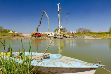 Endüstriyel kule sondaj makinesi, yere büyük aletler yığmak. Pompalı kamyonet nehir kıyısındaki köprü temeli için taze beton döküyor..