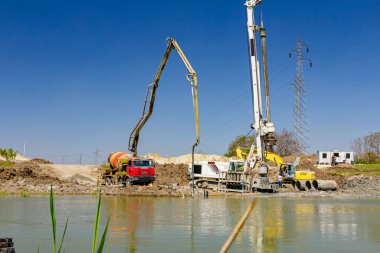 Endüstriyel kule sondaj makinesi, yere büyük aletler yığmak. Pompalı kamyonet nehir kıyısındaki köprü temeli için taze beton döküyor..