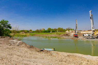 Endüstriyel kule sondaj makinesi, yere büyük aletler yığmak. Pompalı kamyonet nehir kıyısındaki köprü temeli için taze beton döküyor..