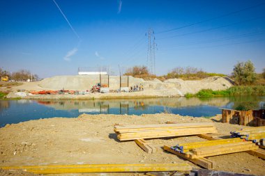 Açık havada depolama yapmak, kalaslar, kirişler yere yığılmış, ahşap profiller bir köprü kalıbı oluşturma ihtiyacı için, nehir boyunca inşaat halindeki köprü direkleridir..