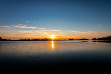 Akşamları güzel günbatımının manzarası gölün üzerinde, gölün üzerinde siluet suyun üzerinde ve bulutların sakin sularda yansıması.