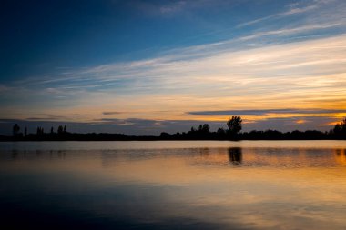 Akşamları güzel günbatımının manzarası gölün üzerinde, gölün üzerinde siluet suyun üzerinde ve bulutların sakin sularda yansıması.