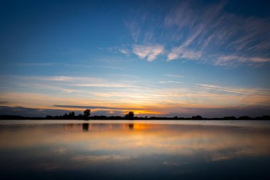 Akşamları güzel günbatımının manzarası gölün üzerinde, gölün üzerinde siluet suyun üzerinde ve bulutların sakin sularda yansıması.