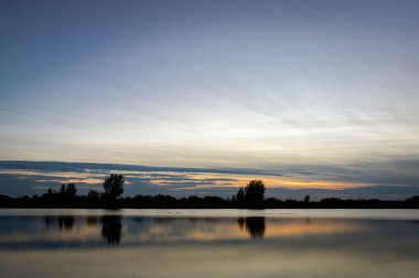 Akşamları güzel günbatımının manzarası gölün üzerinde, gölün üzerinde siluet suyun üzerinde ve bulutların sakin sularda yansıması.