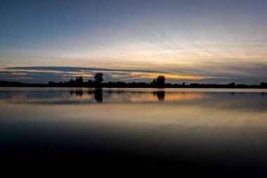 Akşamları güzel günbatımının manzarası gölün üzerinde, gölün üzerinde siluet suyun üzerinde ve bulutların sakin sularda yansıması.