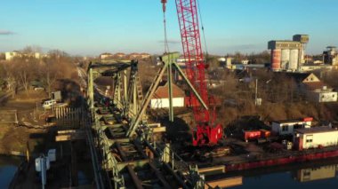 Dolly, nehir kıyısındaki eski demiryolu köprüsünün bir parçası olan hurda metali taşıyıp tutarken büyük vinç etrafında hareket eder..