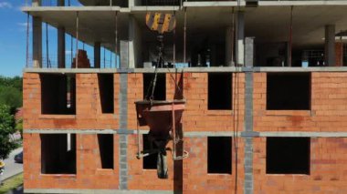 Yukarıda, kule vinci yukarı doğru koni tankı kaldırıyor, konik metal kova beton karışımını taşımak ve dağıtmak için, inşaat alanının üzerine dökülüyor, yeni tamamlanmamış çok katlı bina.