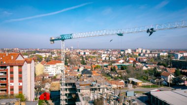Birkaç bağlı beton ağırlıktan oluşan dengesi olan vinç konsolunun üstünde yük tarafından sallanan kafes kirişleri, açık mavi gökyüzü olan şehir manzarası..