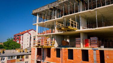 İşçi yardım eder, dengeyi ve istikameti korur, el yapımı iskele üzerindeki kırmızı blokları taşımaya devam eder, güçlü ahşap kalaslardan, malzeme platformundan yapılmış, yapının en üst katına yerleştirilir..