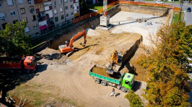 Kazı yaparken iki büyük kazıcının üstünde, yeni konut binası için kazı yapıyorlar ve birkaç çöp kamyonunu toprakla dolduruyorlar, inşaat alanında, proje devam ediyor.