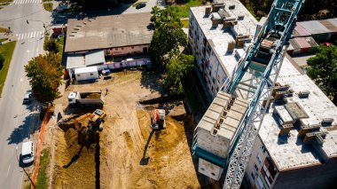 İki kazıcının kazı yaptığı, konut inşaatı için temel kazdığı ve birkaç çöp kamyonunu inşaat alanında zemin ile doldurduğu görüşünün üzerinde. Dengeli kule vinci, denge ağırlıkları