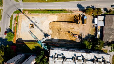 Kazı yaparken iki büyük kazıcının üstünde, yeni konut binası için temel kazıyorlar ve birkaç çöp kamyonunu toprakla dolduruyorlar, inşaat alanında, proje devam ediyor.
