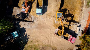 Kazı yaparken iki büyük kazıcının üstünde, yeni konut binası için temel kazıyorlar ve birkaç çöp kamyonunu toprakla dolduruyorlar, inşaat alanında, proje devam ediyor.