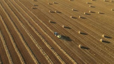 Manzaranın üstünde, çekici traktörün üzerinde yuvarlak balyayı çekerken, kamışı yuvarlayan ve tarımsal alanın üzerine doldurulmuş yuvarlak bir balya tüküren makine..