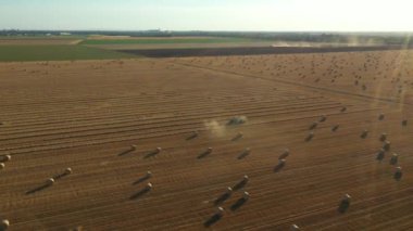 Dolly yukarıda, traktörün etrafındaki ışıkla yörüngeyi hareket ettirir. Pipeti yuvarlayan ve tarımsal alanın üzerine yuvarlanmış yuvarlak bir balya püskürten makine gibi..