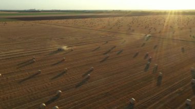 Manzaranın üstünde, kukla iki traktörün etrafındaki arka ışıkla yörüngede hareket eder, makineler kamışı yuvarlar ve tarımsal alanın üzerine dolu bir balya püskürtür, birlikte çalışırlar..