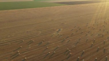 Dolly yukarıda, traktörün etrafındaki ışıkla yörüngeyi hareket ettirir. Pipeti yuvarlayan ve tarımsal alanın üzerine yuvarlanmış yuvarlak bir balya püskürten makine gibi..