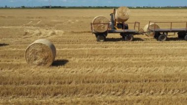 Kazıcının üstünde, karavana saman balyaları yüklerken, tarla arazisinde traktörle çekilirken, forklift bıçağı ve ek taşıyıcı kullanarak,.