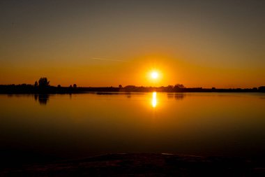 Akşamları güzel günbatımının manzarası gölün üzerinde, gölün üzerinde siluet suyun üzerinde ve bulutların sakin sularda yansıması.