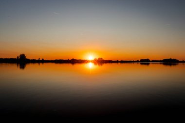 Akşamları güzel günbatımının manzarası gölün üzerinde, gölün üzerinde siluet suyun üzerinde ve bulutların sakin sularda yansıması.