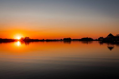 Akşamları güzel günbatımının manzarası gölün üzerinde, gölün üzerinde siluet suyun üzerinde ve bulutların sakin sularda yansıması.