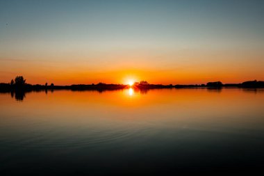 Akşamları güzel günbatımının manzarası gölün üzerinde, gölün üzerinde siluet suyun üzerinde ve bulutların sakin sularda yansıması.
