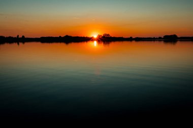 Akşamları güzel günbatımının manzarası gölün üzerinde, gölün üzerinde siluet suyun üzerinde ve bulutların sakin sularda yansıması.