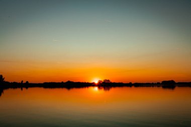 Akşamları güzel günbatımının manzarası gölün üzerinde, gölün üzerinde siluet suyun üzerinde ve bulutların sakin sularda yansıması.