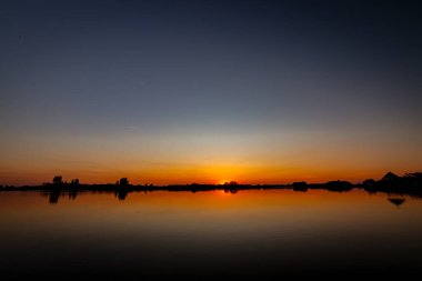 Akşamları güzel günbatımının manzarası gölün üzerinde, gölün üzerinde siluet suyun üzerinde ve bulutların sakin sularda yansıması.