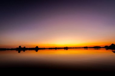 Akşamları güzel günbatımının manzarası gölün üzerinde, gölün üzerinde siluet suyun üzerinde ve bulutların sakin sularda yansıması.