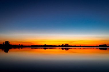Akşamları güzel günbatımının manzarası gölün üzerinde, gölün üzerinde siluet suyun üzerinde ve bulutların sakin sularda yansıması.
