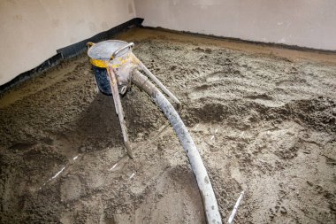 Pompa makinesi çimento ve kum karışımını atar, yarı kuru zemin perdelenmiş karışım, ince boruların üzerine dökülür, inşaat halindeki konut binasında yer altı ısıtma için dağıtım sistemi.