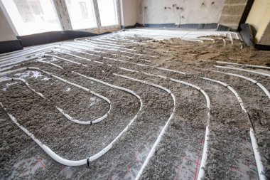 Yarı kuru zemin çimento ve kum karışımı ince beyaz tüpler üzerine dökülüyor. İnşaat halindeki konut binasında zemin altı ısıtma için karmaşık dağıtım sisteminde bükülüyor..