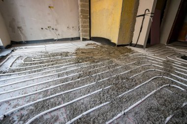 Yarı kuru zemin çimento ve kum karışımı ince beyaz tüpler üzerine dökülüyor. İnşaat halindeki konut binasında zemin altı ısıtma için karmaşık dağıtım sisteminde bükülüyor..