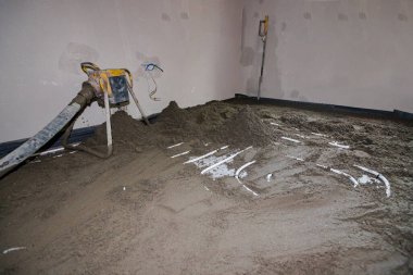 Pompa makinesi çimento ve kum karışımını atar, yarı kuru zemin perdelenmiş karışım, ince boruların üzerine dökülür, inşaat halindeki konut binasında yer altı ısıtma için dağıtım sistemi.