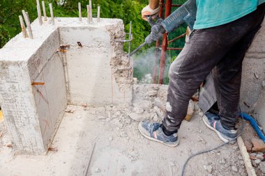 İnşaat işçisi, güçlendirilmiş betonu yeniden hizalamak için elektrikli matkap kullanıyor. İnşaat halindeki konut binasının balkon çitlerinin üzerinde taşkınlık yapıyor, kaldırıyor, yıkıyor..