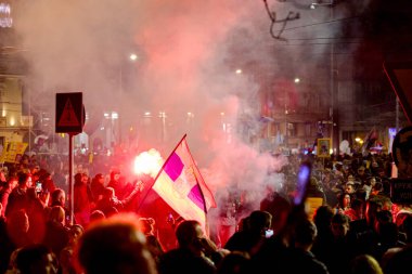Belgrad, Sırbistan - 15 Mart 2025: Elinde yanan fişek tutan kalabalıktan bir adam, kırmızı meşaleyi mor, kırmızı duman çıkarırken yaktı. Öğrenciler, vatandaşlar hükümete ve rejime karşı protesto