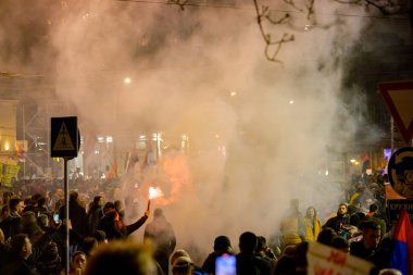 Belgrad, Sırbistan - 15 Mart 2025: Elinde yanan fişek tutan kalabalıktan bir adam, kırmızı meşaleyi mor, kırmızı duman çıkarırken yaktı. Öğrenciler, vatandaşlar hükümete ve rejime karşı protesto