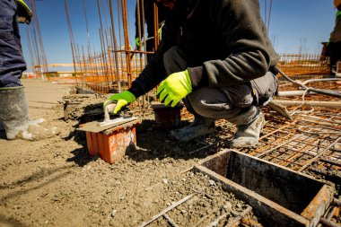 İşçi küp kalıbını betonla doldurmak için mala kullanıyor, gerilme ya da esneklik testi için örnek alıyor ve çimento karışımı döküm yapım temellerinin sıkıştırıcı güç testi yapıyor. Üst yüzeyi bitirmek için mala kullan.