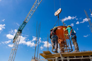 İnşaat işçileri konik metal kovaları boşaltıyorlar, taşınıyor ve beton karışımını yüksek tutuyorlar, binanın sütunları için dikey kalıba beton döküyorlar, koni tankını taşırken vinç kullanıyorlar..
