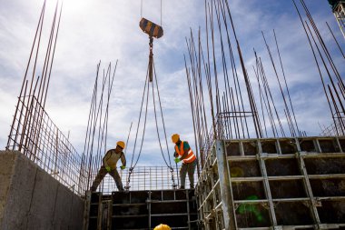 Kule vinci, çelik yelek ve miğferli inşaat işçilerinin güçlendirilmiş beton sütun için uzun tahta sökülebilir büyük küf yapmalarına yardımcı olur..