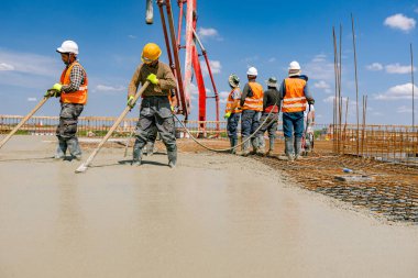 İnşaat işçileri el yapımı aletleri dikdörtgen armatür üzerine döküp, taze betonu düzleştiriyorlar..